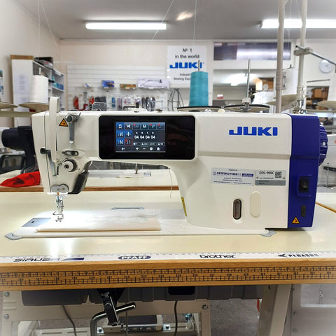 Juki DDL900C Plain Sewing Machine with thread trimmer and foot lift, displayed in a workshop setting with a piece of fabric and a needle attached.