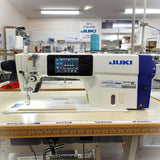 Juki DDL900C Plain Sewing Machine with thread trimmer and foot lift, displayed in a workshop setting with a piece of fabric and a needle attached.