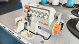A close-up, perspective view of a Siruba 767Q industrial overlock sewing machine with five thread tension dials and a piece of fabric ready for stitching.