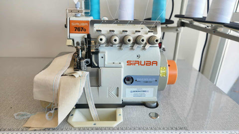 A high-angle shot of a Siruba industrial sewing machine showing teal and white thread spools connected through the overhead guide system.